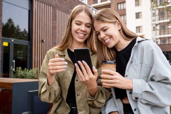 Young twin sisters in casualwear looking at smartphone screen